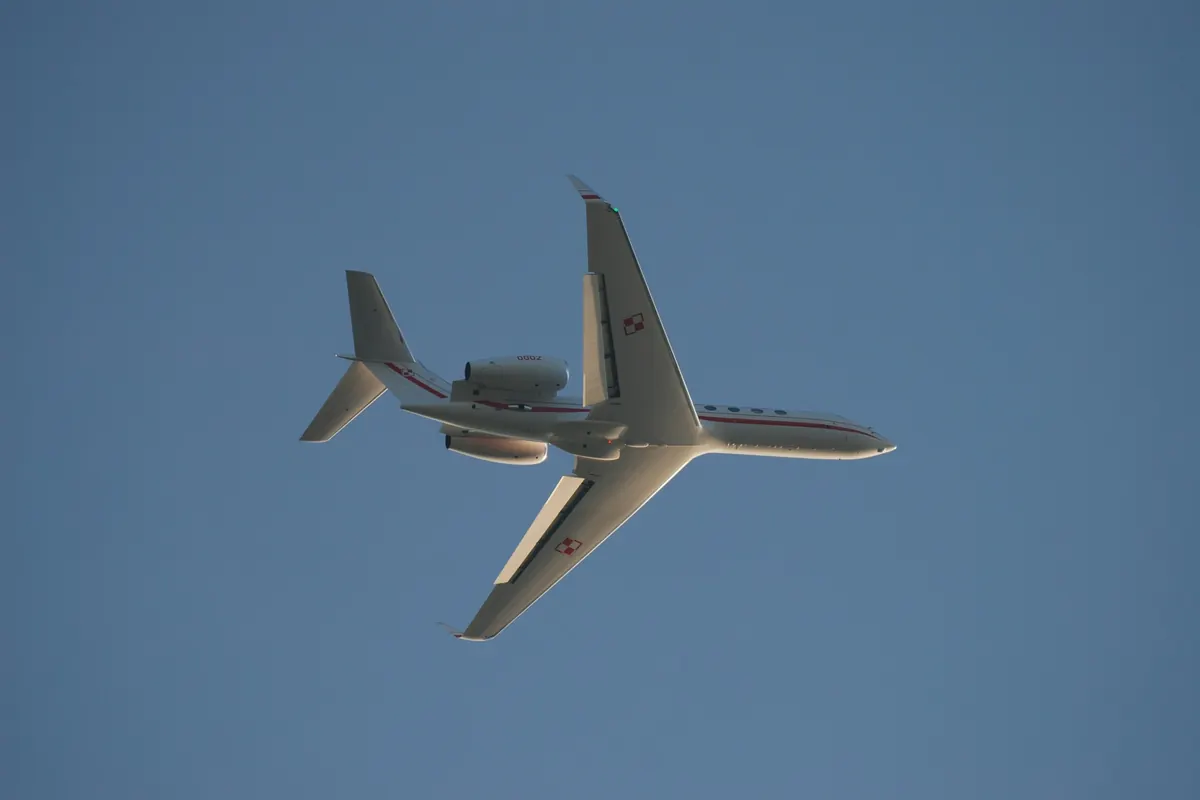 Business jet overhead with gear down against a pale sky
